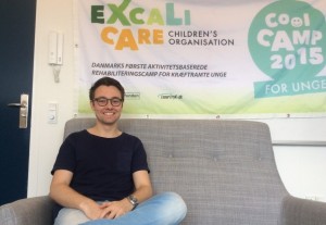 Billede af ExcaliCare's Rasmus Thøger Christensen siddende i en sofa med ExcaliCare's banner bag sig